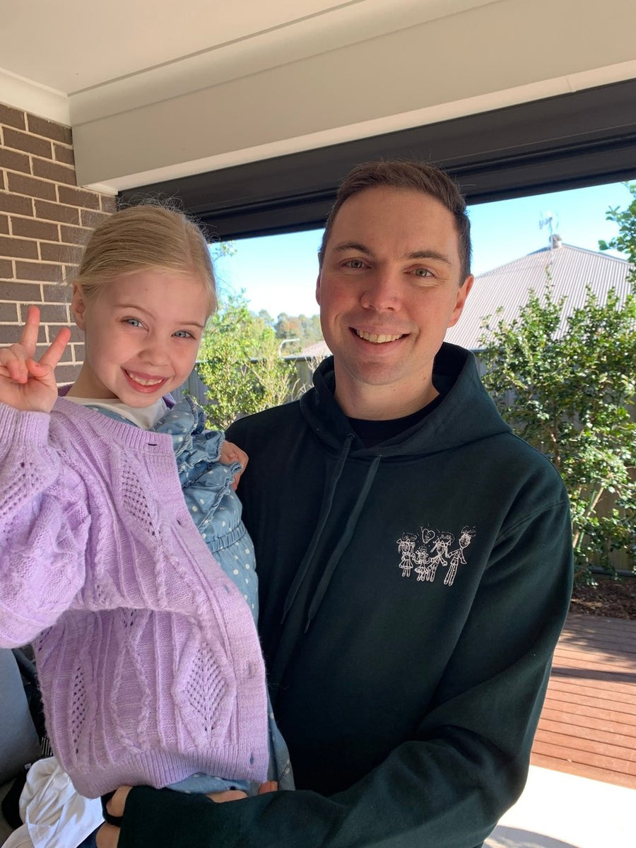 Dad wearing his kids drawing embroidered hoodie holding his daughter