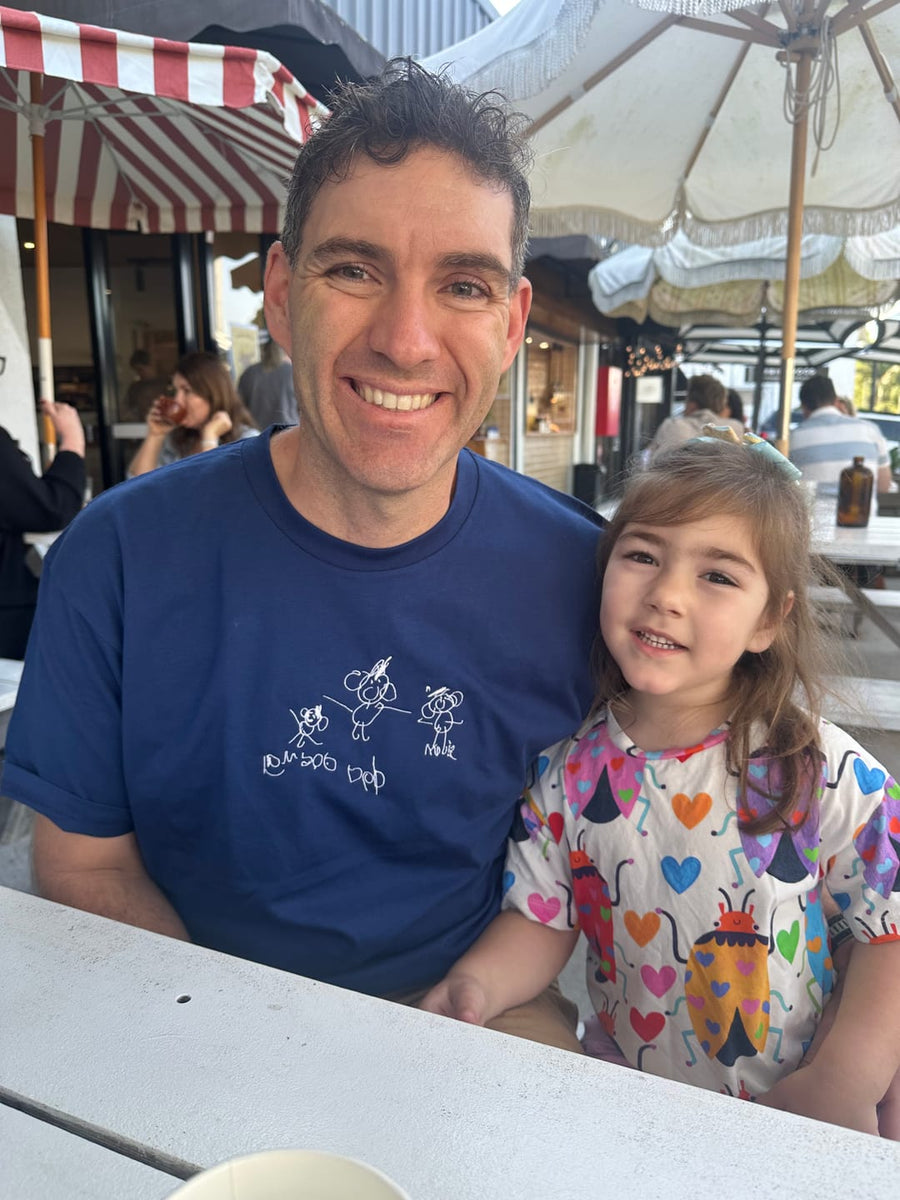 A dad in a black hoodie machine embroidered with his child's drawing, holding his daughter